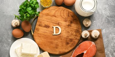 Top view of foods rich in vitamin D, including salmon, eggs, cheese, mushrooms, milk, and supplements, arranged around a wooden board with the letter "D"—ideal for illustrating a concept related to vitamin D analysis in nutrition and food science.