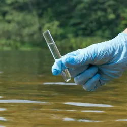 Sample water from the river for analysis. Hand in glove holding a test tube.