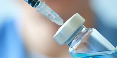 Close-up of a doctor's hand holding a syringe and vaccine vial, symbolizing the final fill-finish stage of the vaccine manufacturing process in a clinical setting.