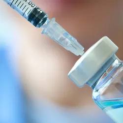 Close-up of a doctor's hand holding a syringe and vaccine vial, symbolizing the final fill-finish stage of the vaccine manufacturing process in a clinical setting.