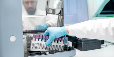 Laboratory technician placing test tubes into an automated analyzer for vaccine stability testing.