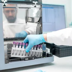 Laboratory technician placing test tubes into an automated analyzer for vaccine stability testing.