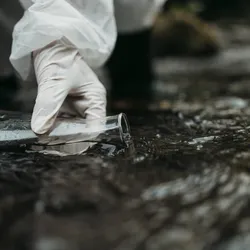 Gloved hand extracting water sample from river in a conical flask