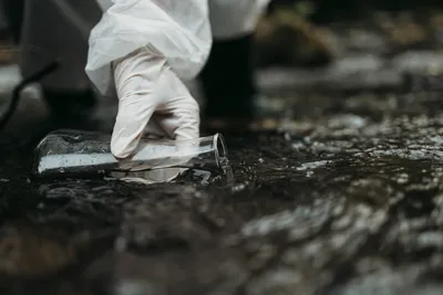 Gloved hand extracting water sample from river in a conical flask