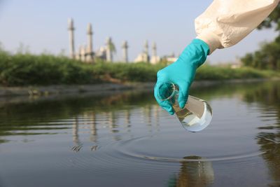 surgical gloved hand holding conical flask to collect water samples