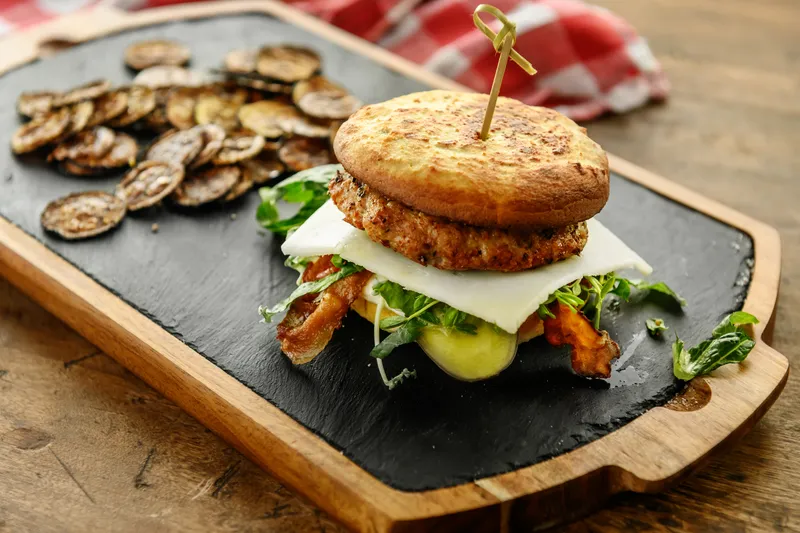 Plant-based burger with cheese, greens, and roasted vegetables on a wooden serving board, representing alternative protein products analyzed for nutrition and flavor using GC/MS.