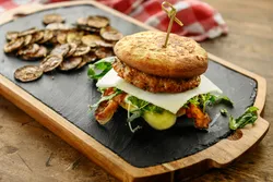 Plant-based burger with cheese, greens, and roasted vegetables on a wooden serving board, representing alternative protein products analyzed for nutrition and flavor using GC/MS.