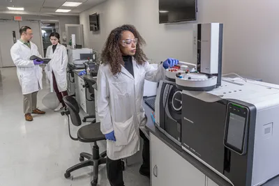 Scientist operating an automated GC–MS/MS system in a modern laboratory, preparing vials for trace contaminant and PFAS analysis.