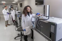 Scientist operating an automated GC–MS/MS system in a modern laboratory, preparing vials for trace contaminant and PFAS analysis.