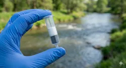 A gloved hand holds a dual-layer solid-phase extraction cartridge against a river background, illustrating the advanced technology used for environmental SVOC analysis.