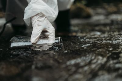 Gloved hand extracting water sample from river in a conical flask