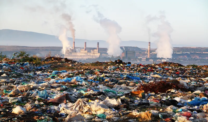 Smoke stacks in background showing pollution over a landfill site.