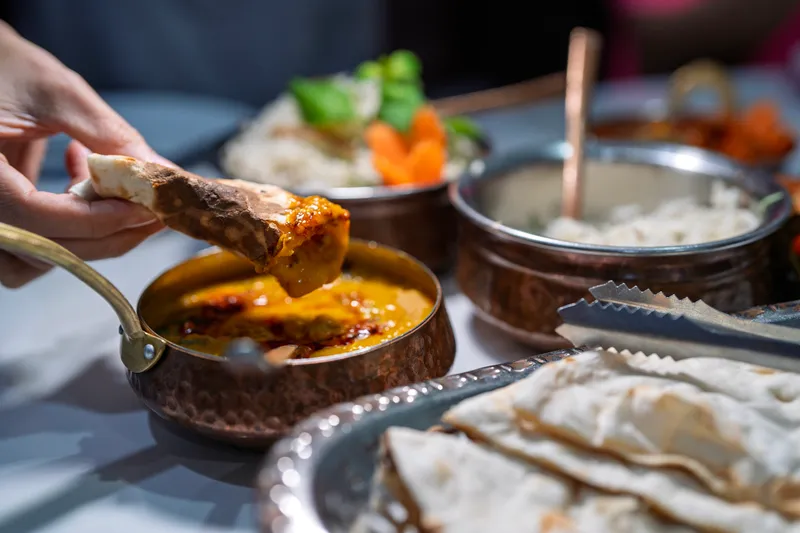 A hand dipping naan into a sauce, representing food allergen testing challenges.