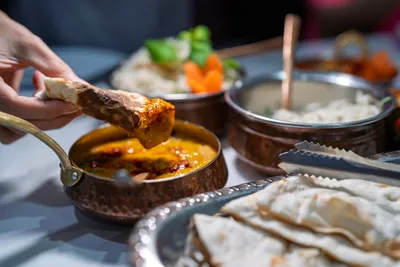 A hand dipping naan into a sauce, representing food allergen testing challenges.