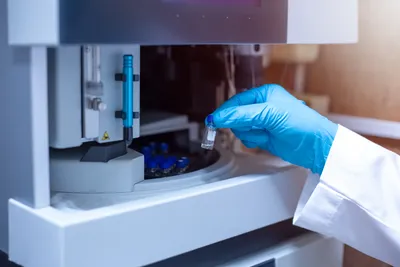 Laboratory analyst loading a sample vial into a mass spectrometer during PFAS degradation pathway analysis using advanced analytical instrumentation.