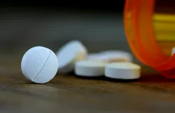 Close-up of white aspirin tablets spilling from an orange prescription bottle, illustrating acetylsalicylic acid peak fronting issues discussed in liquid chromatography method development under USP-like conditions.