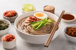 Soba noodle bowl accompanied by kimchi and condiments