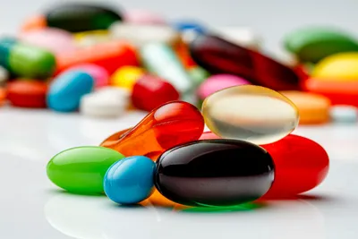 Assorted colorful pharmaceutical pills and capsules on a white surface, representing the expanding pipeline of accessible therapeutics driven by Next-Generation Biosimilar Development.