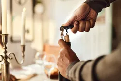 Person opening a wine bottle with a corkscrew representing real-time mass spectrometry use cases.