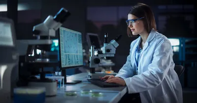 A bioprocess researcher wearing safety glasses analyzes experimental data from mixed-mode chromatography on a laboratory computer.