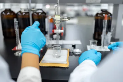 Laboratory technician performing classical column chromatography sample preparation using a glass benchtop column to fractionate crude sample prior to LC-MS analysis.