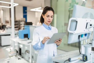 Scientist using a digital tablet to monitor integrated CDS and LIMS automated chromatography workflows in a modern laboratory.