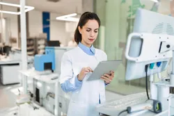 Scientist using a digital tablet to monitor integrated CDS and LIMS automated chromatography workflows in a modern laboratory.