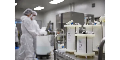 GMP cleanroom with multiple white prepacked chromatography columns arranged on a stainless steel skid in the foreground, with two fully gowned technicians working in the background.
