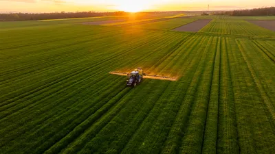Aerial view of a tractor spraying pesticide in farm fields
