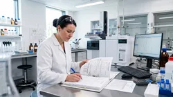 An analyst reviewing GC method validation documentation at a laboratory bench with a gas chromatograph in the background.