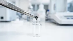 Tweezers holding a sample material above a vial for moisture analysis in lithium battery testing.