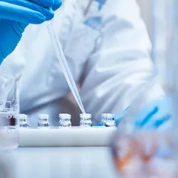 Scientist filling vials with solution through pipette in test tube rack. Chemist is examining medicine during scientific experiment. She is wearing gloves at pharmaceutical factory.