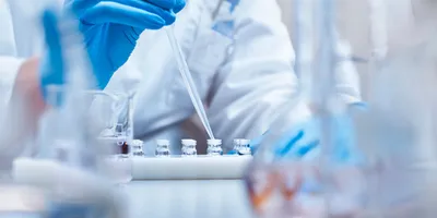 Scientist filling vials with solution through pipette in test tube rack. Chemist is examining medicine during scientific experiment. She is wearing gloves at pharmaceutical factory.

