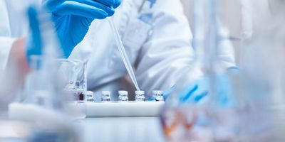 Scientist filling vials with solution through pipette in test tube rack. Chemist is examining medicine during scientific experiment. She is wearing gloves at pharmaceutical factory.

